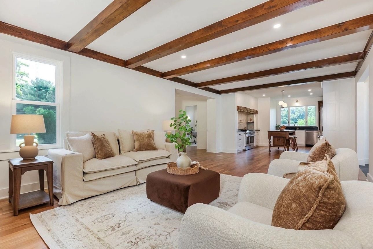 Cream seating, a brown ottoman and exposed wood ceiling beams in a Granville living room